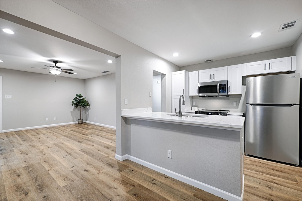 kitchen with stainless steel appliances, sink, white cabinets, and light hardwood / wood-style floors