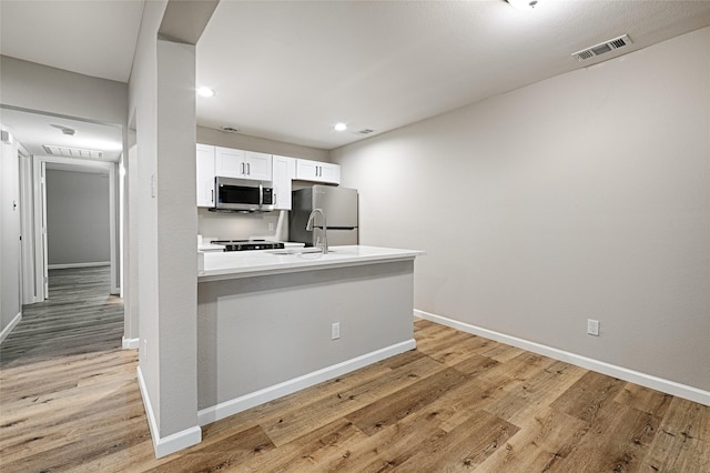 kitchen featuring appliances with stainless steel finishes, white cabinetry, sink, kitchen peninsula, and light hardwood / wood-style flooring