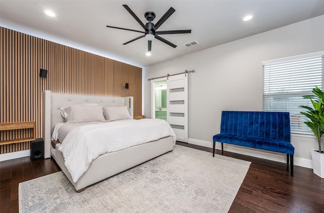 bedroom with a barn door, dark hardwood / wood-style floors, connected bathroom, and ceiling fan