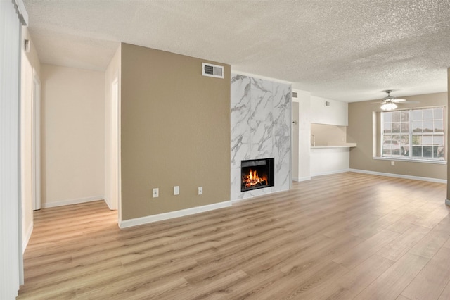 unfurnished living room with ceiling fan, a high end fireplace, light hardwood / wood-style floors, and a textured ceiling