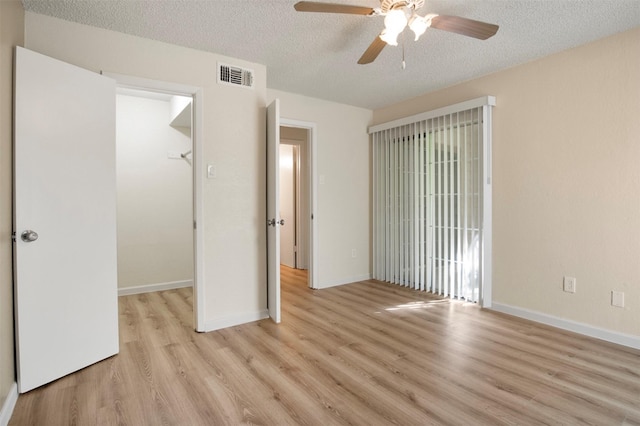 unfurnished bedroom with a walk in closet, access to outside, a textured ceiling, and light hardwood / wood-style flooring