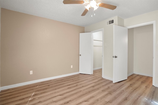 unfurnished bedroom with a walk in closet, a textured ceiling, light wood-type flooring, a closet, and ceiling fan