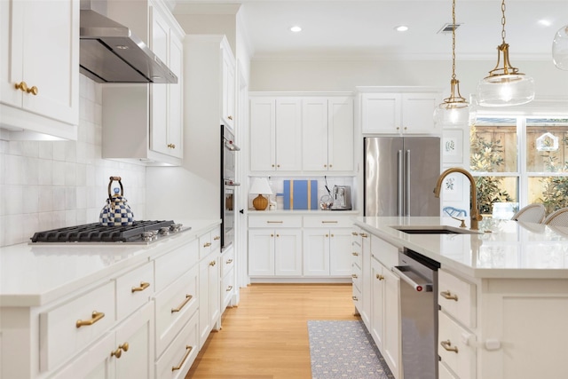 kitchen with pendant lighting, sink, a kitchen island with sink, stainless steel appliances, and wall chimney exhaust hood