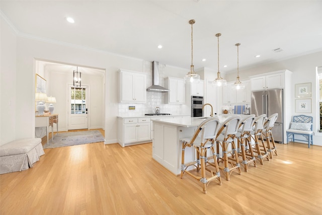 kitchen with white cabinetry, appliances with stainless steel finishes, pendant lighting, and wall chimney range hood