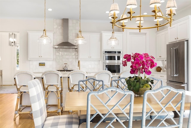 kitchen featuring crown molding, hanging light fixtures, stainless steel appliances, white cabinets, and wall chimney exhaust hood