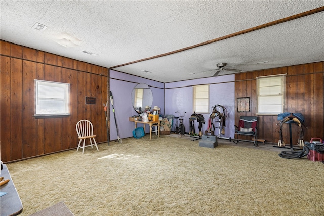 interior space with ceiling fan, carpet, wooden walls, and a textured ceiling