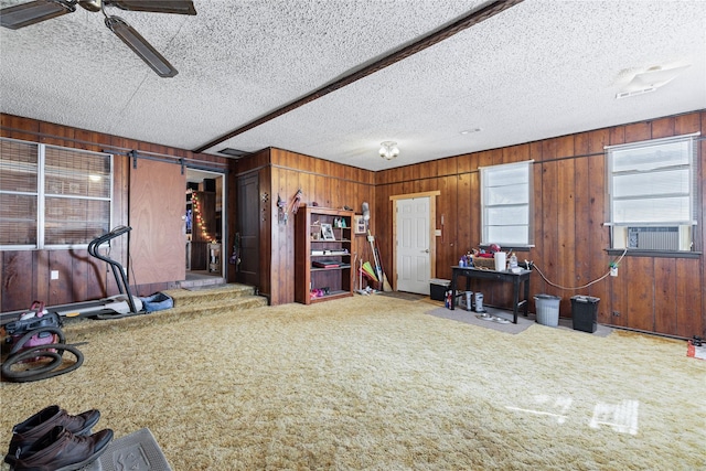 misc room featuring ceiling fan, carpet floors, wooden walls, and a textured ceiling