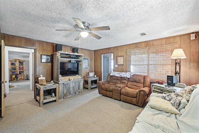 living room featuring ceiling fan, wooden walls, light colored carpet, and a textured ceiling