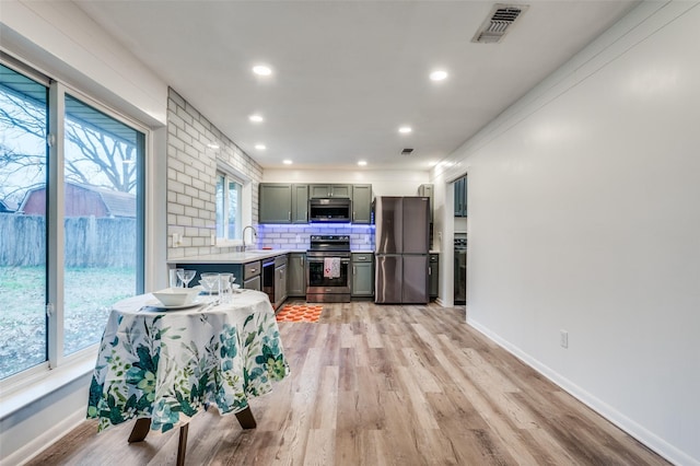 kitchen with tasteful backsplash, stainless steel appliances, sink, and light wood-type flooring