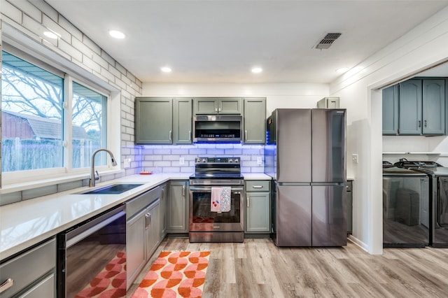 kitchen featuring sink, stainless steel appliances, light hardwood / wood-style floors, washer and dryer, and decorative backsplash