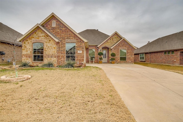 french country home featuring stone siding, brick siding, and roof with shingles