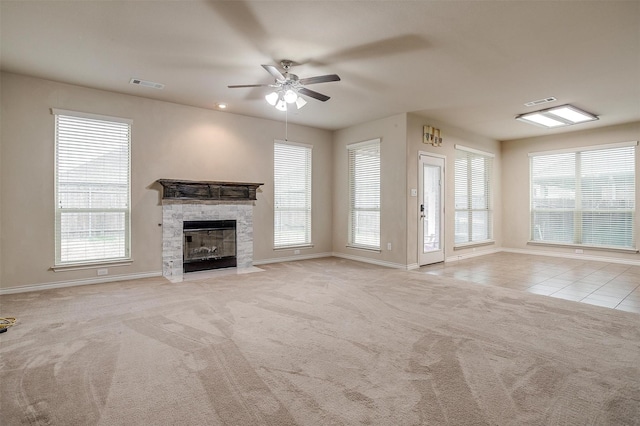 unfurnished living room featuring a wealth of natural light, a stone fireplace, light carpet, and ceiling fan