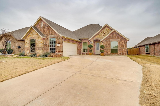 view of front of property featuring brick siding, a shingled roof, concrete driveway, an attached garage, and stone siding