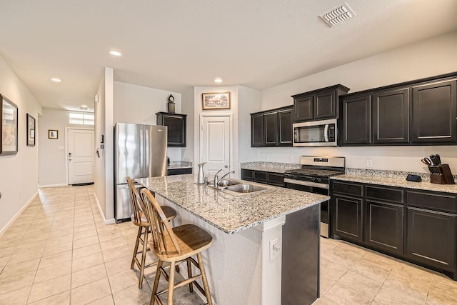 kitchen featuring appliances with stainless steel finishes, sink, a kitchen island with sink, light tile patterned floors, and light stone countertops