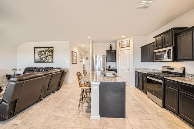 kitchen with sink, appliances with stainless steel finishes, a kitchen breakfast bar, light stone counters, and an island with sink