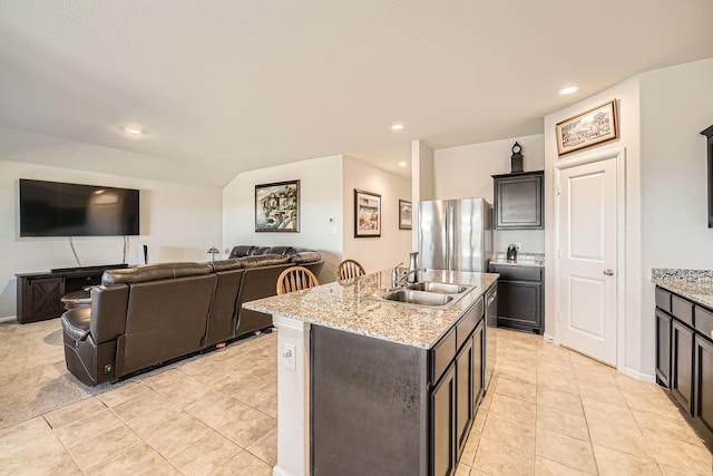 kitchen featuring stainless steel appliances, an island with sink, sink, and light stone counters