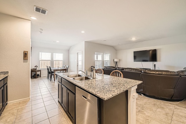 kitchen with sink, stainless steel dishwasher, light tile patterned floors, light stone countertops, and a center island with sink