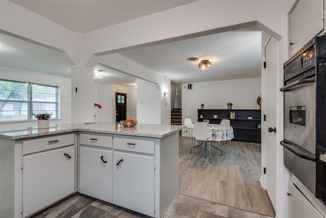 kitchen with kitchen peninsula, light stone countertops, stainless steel oven, and white cabinets