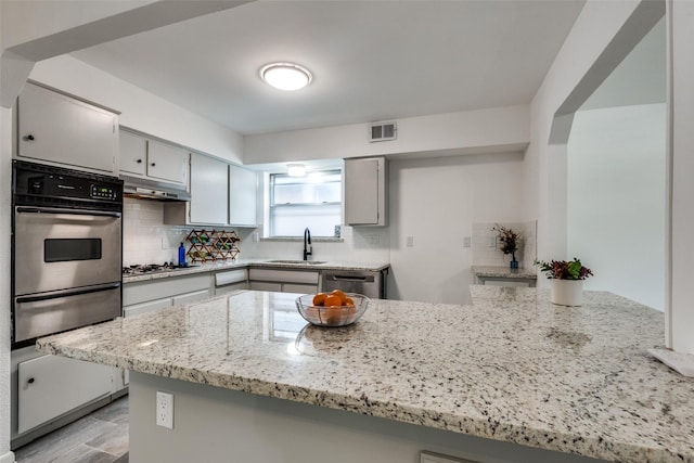 kitchen featuring appliances with stainless steel finishes, tasteful backsplash, sink, light stone counters, and kitchen peninsula