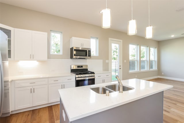 kitchen featuring sink, white cabinetry, stainless steel appliances, an island with sink, and decorative light fixtures