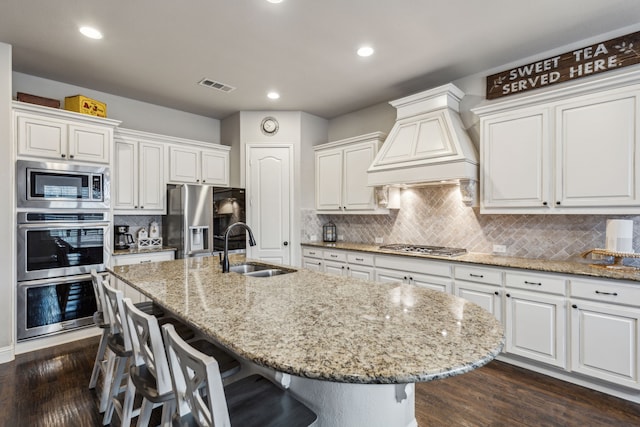 kitchen featuring premium range hood, stainless steel appliances, sink, and a kitchen island with sink