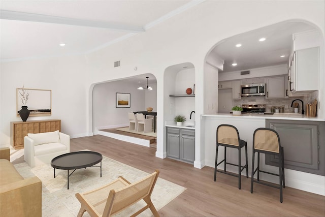 living area featuring visible vents, arched walkways, light wood-style flooring, and ornamental molding