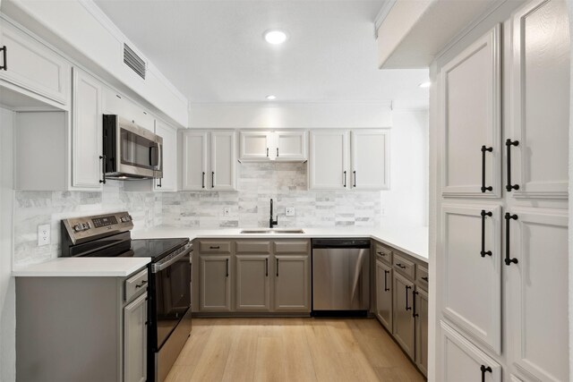 kitchen with tasteful backsplash, appliances with stainless steel finishes, gray cabinetry, and light hardwood / wood-style floors