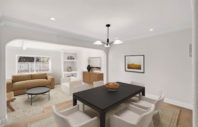 dining room with built in shelves, ornamental molding, a chandelier, and light wood-type flooring