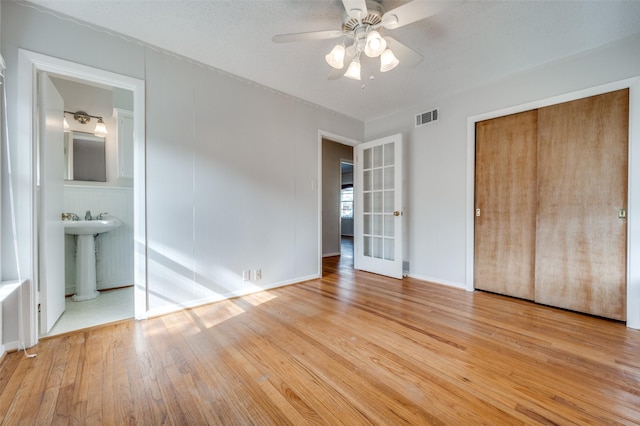 unfurnished bedroom with connected bathroom, sink, light wood-type flooring, a closet, and ceiling fan