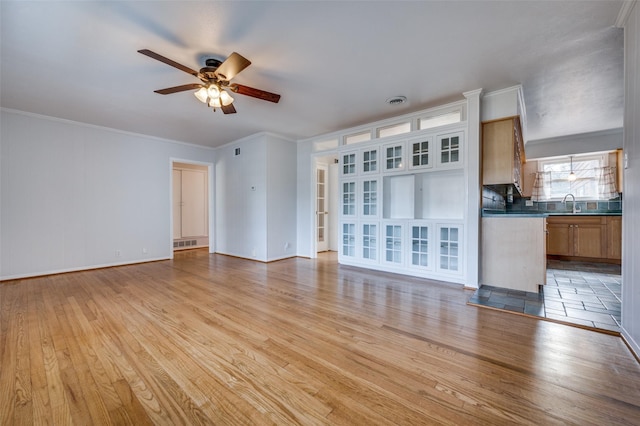 unfurnished living room featuring ceiling fan, ornamental molding, sink, and light hardwood / wood-style flooring