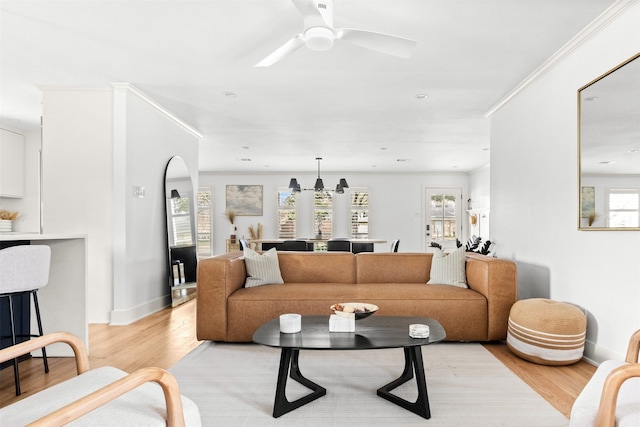 living room featuring crown molding, built in features, ceiling fan, a brick fireplace, and light wood-type flooring