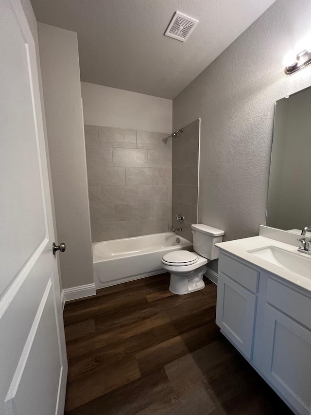 full bathroom with hardwood / wood-style flooring, vanity, tiled shower / bath combo, and toilet