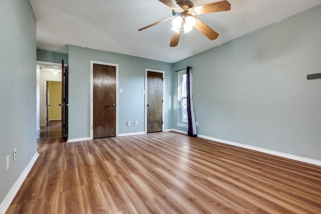 unfurnished bedroom with wood-type flooring, two closets, ceiling fan, and a textured ceiling