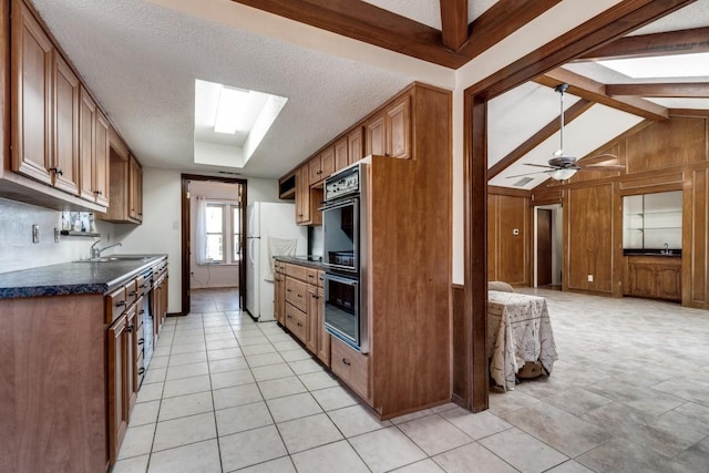 kitchen with wooden walls, lofted ceiling with skylight, black double oven, white refrigerator, and a textured ceiling