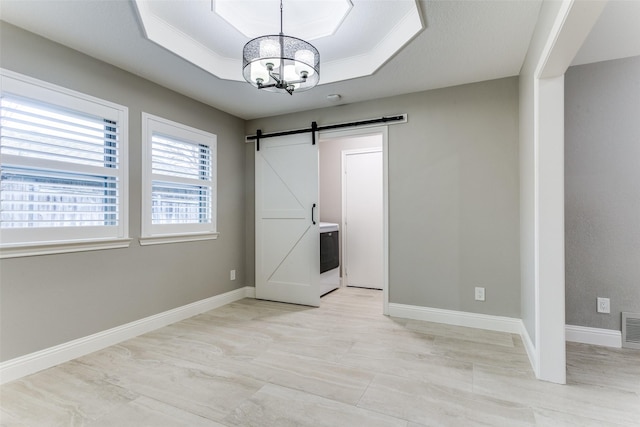 interior space featuring an inviting chandelier, a tray ceiling, and a barn door