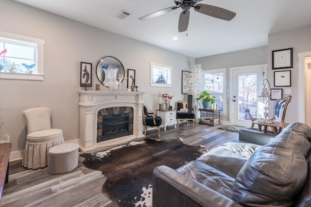 living area featuring visible vents, a ceiling fan, a glass covered fireplace, wood finished floors, and baseboards