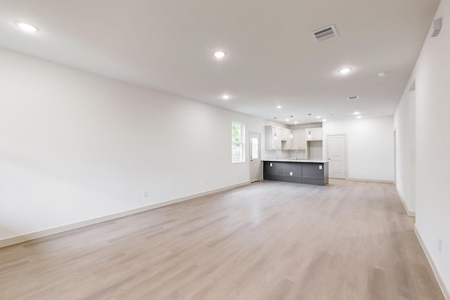 unfurnished living room featuring recessed lighting, visible vents, a sink, light wood-type flooring, and baseboards