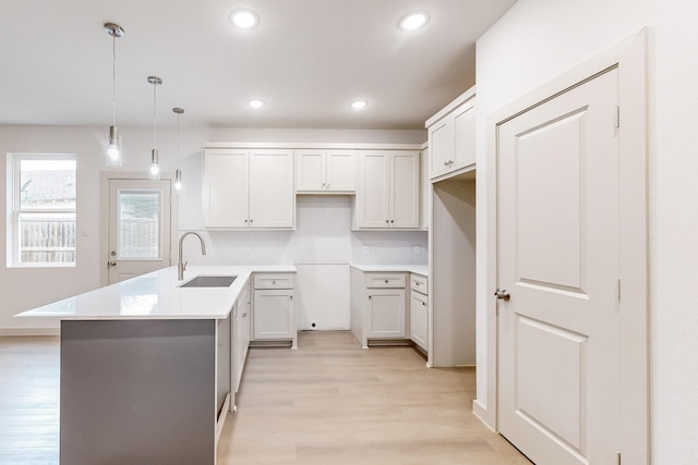 kitchen featuring a peninsula, a sink, white cabinets, light countertops, and pendant lighting