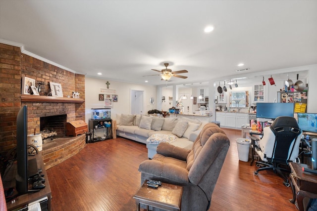 living room featuring hardwood / wood-style flooring, ceiling fan, crown molding, and a brick fireplace