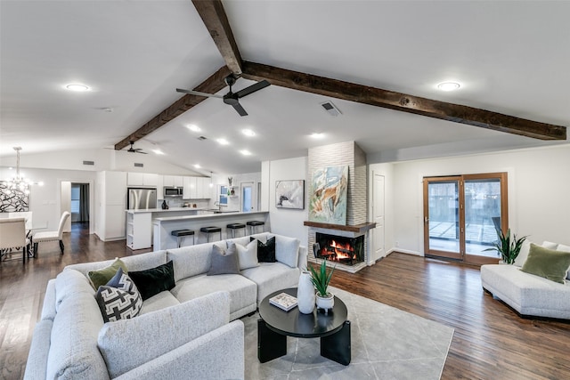 living room with dark hardwood / wood-style floors, a fireplace, ceiling fan with notable chandelier, and lofted ceiling with beams