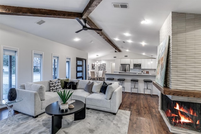 living room with ceiling fan with notable chandelier, lofted ceiling with beams, a large fireplace, and hardwood / wood-style flooring