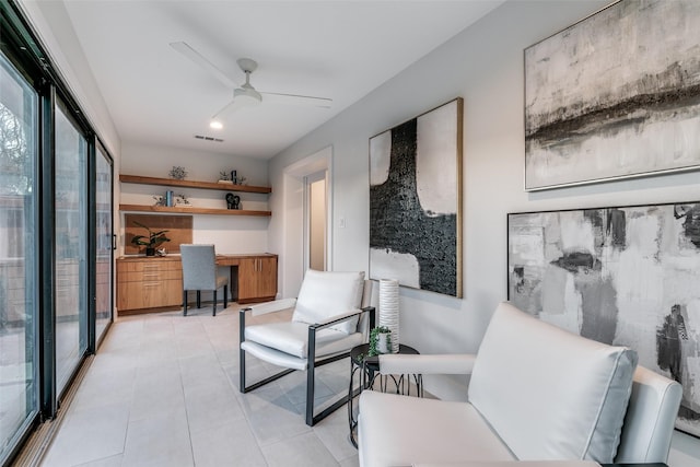 living area featuring built in desk, ceiling fan, and light tile patterned flooring