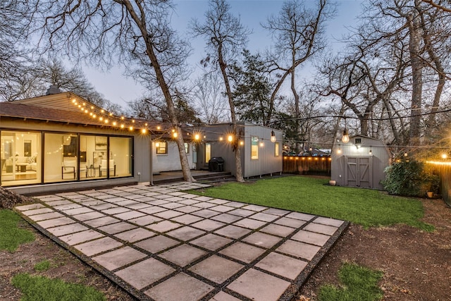 back house at dusk with a lawn, a shed, and a patio area