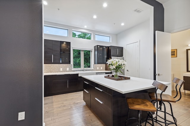 kitchen with a kitchen island, a breakfast bar, sink, decorative backsplash, and light hardwood / wood-style flooring