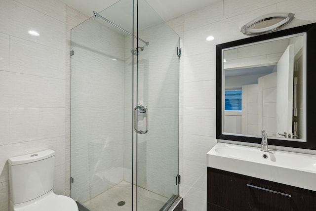 bathroom featuring a shower with door, vanity, tile walls, and toilet