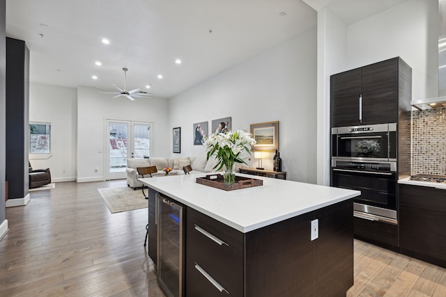 kitchen with beverage cooler, light wood-type flooring, a kitchen island, and wall chimney range hood