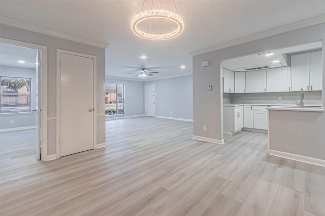 unfurnished living room featuring crown molding, ceiling fan with notable chandelier, a wealth of natural light, and light wood-type flooring