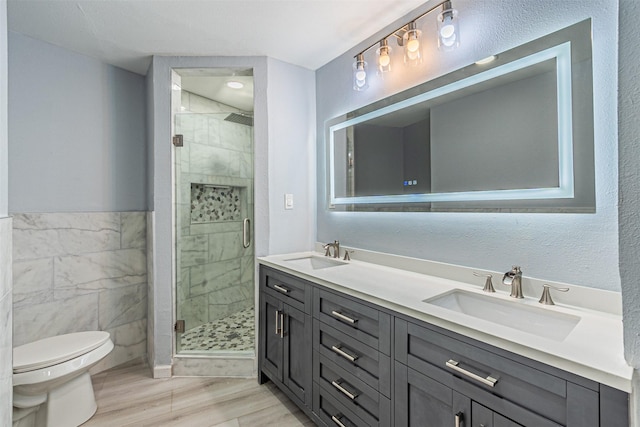 bathroom with tile walls, hardwood / wood-style flooring, vanity, toilet, and a shower with door