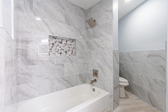 bathroom featuring tiled shower / bath, tile walls, and toilet