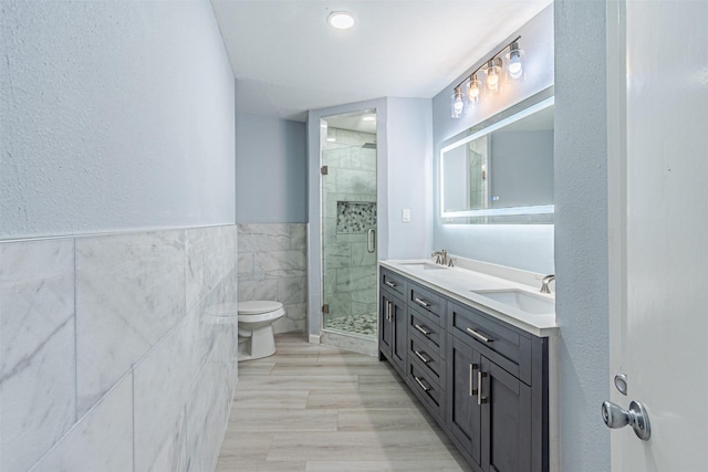 bathroom with vanity, toilet, a shower with door, and tile walls